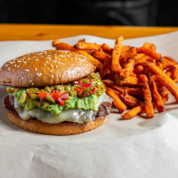 Skirted Heifer burger with guacamole, peppers, melted cheese, and a side of sweet potato fries.