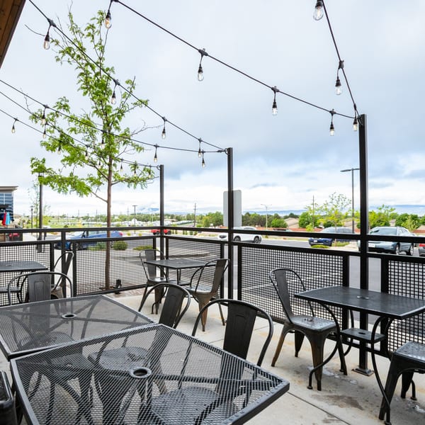 Outdoor patio at Skirted Heifer with metal tables and chairs, string lights, and a tree.