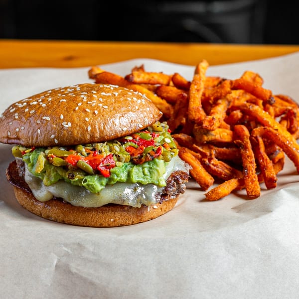 Skirted Heifer burger with guacamole, melted cheese, and roasted peppers, served with sweet potato fries.