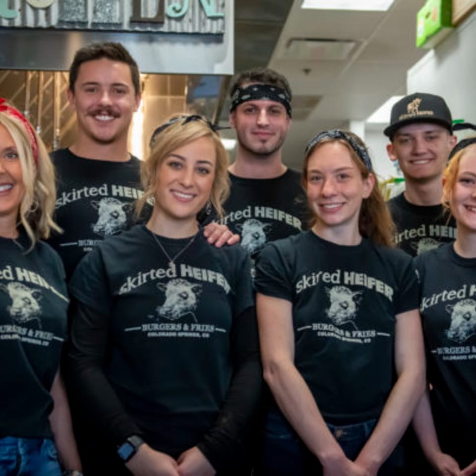 Smiling Skirted Heifer staff in black t-shirts with a cow logo stand together in the kitchen.