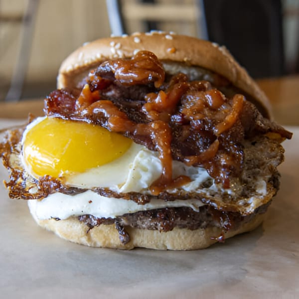 Skirted Heifer burger with a fried egg, caramelized onions, and bacon on a sesame seed bun.