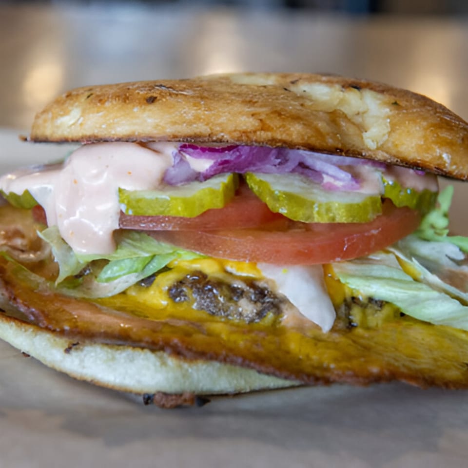 Close-up of a Skirted Heifer burger with melted cheese, lettuce, tomato, pickles, red onion, and sauce.
