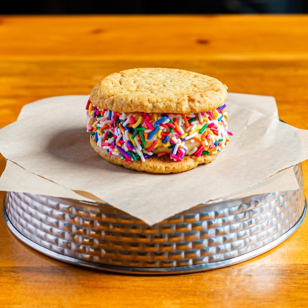 Oatmeal cookie ice cream sandwich with colorful sprinkles on a metal tray.