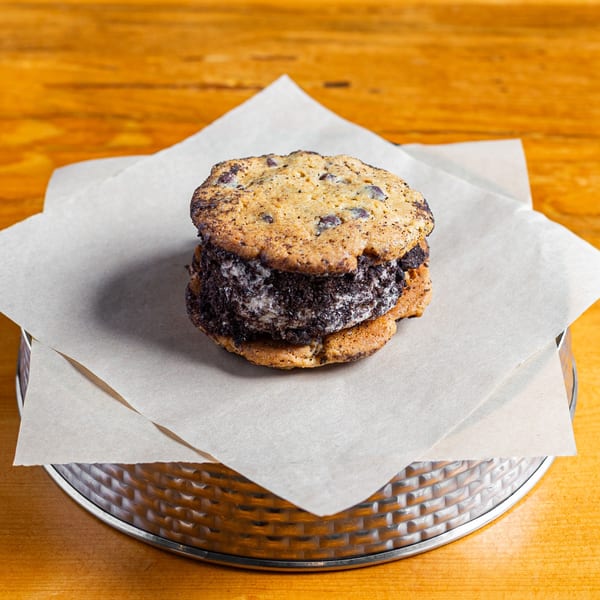 A Skirted Heifer chocolate chip cookie ice cream sandwich on parchment paper and a metal tray.