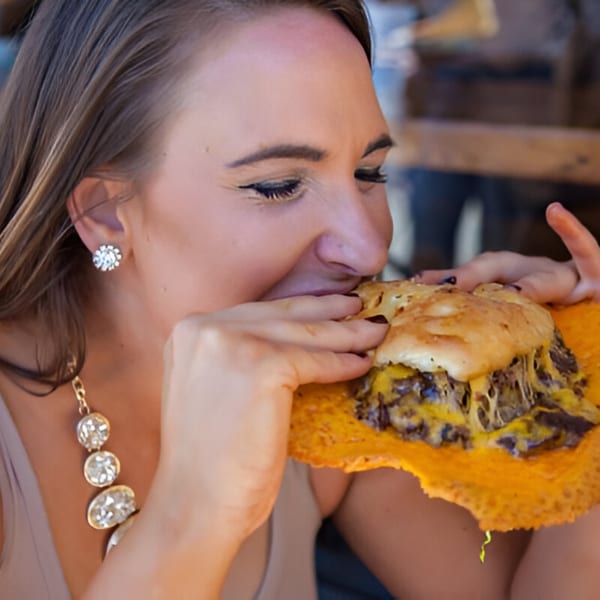 A woman eagerly bites into a Skirted Heifer burger, featuring a crispy cheese skirt.