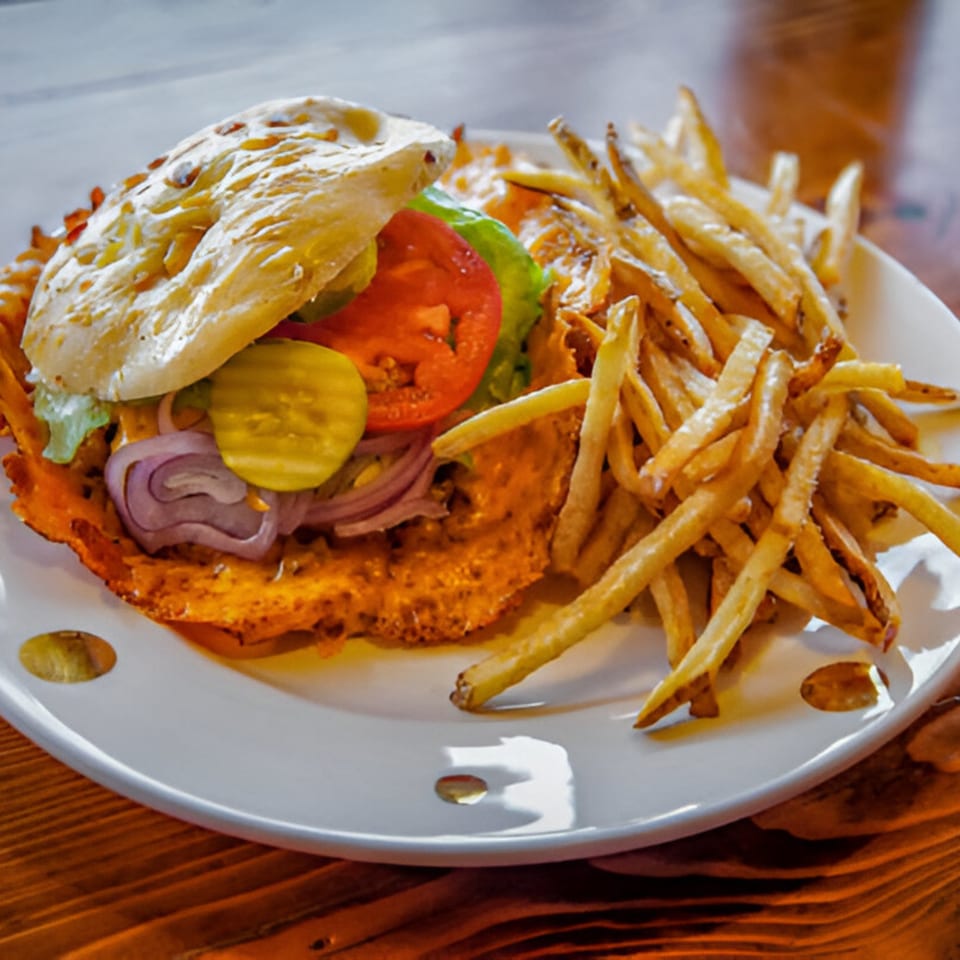 A Skirted Heifer burger with lettuce, tomato, onions, and pickles, served with a side of fries.