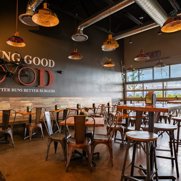 Interior of Skirted Heifer restaurant with industrial lighting, wooden tables, metal chairs, and large windows.