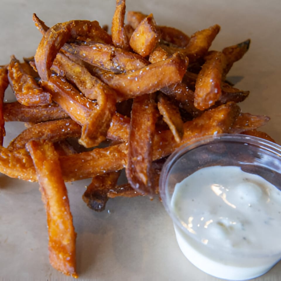 A pile of crispy sweet potato fries with a side of creamy dipping sauce.