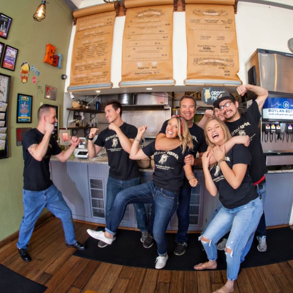Six Skirted Heifer staff members playfully pose and flex in front of the restaurant's counter and menu.