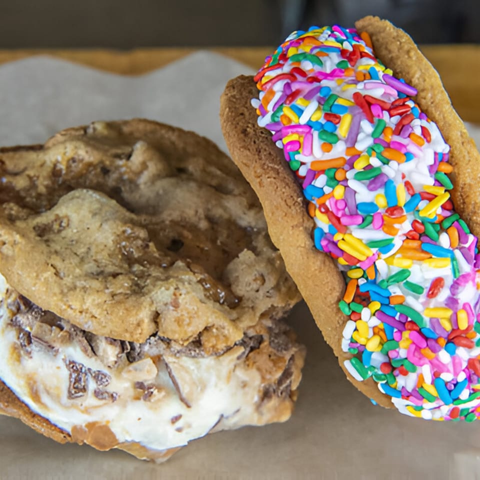 Two ice cream sandwiches, one with toffee bits and one with colorful sprinkles, on parchment paper.