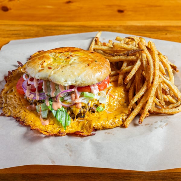 A Skirted Heifer burger with melted cheese, lettuce, tomato, onion, and sauce, served with fries.