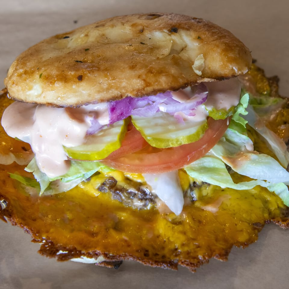 A Skirted Heifer burger with a crispy cheese skirt, lettuce, tomato, pickles, onions, and sauce.