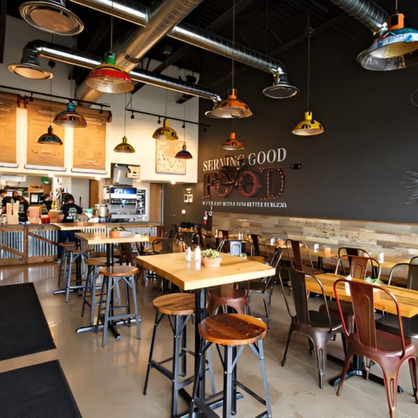 Interior of Skirted Heifer restaurant with high-top tables, bar seating, and a "Serving Good Food" sign.