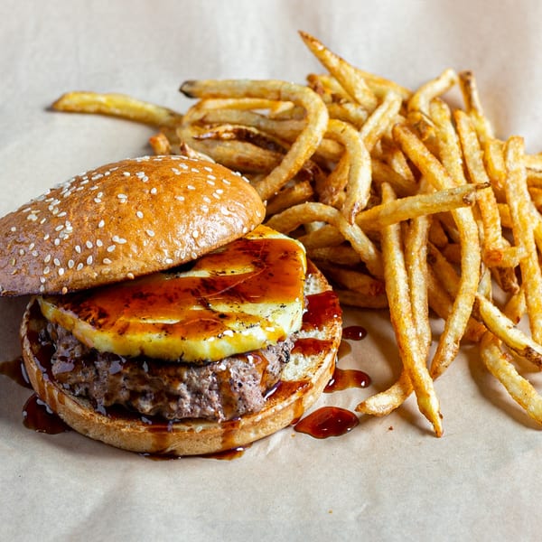A Skirted Heifer burger with grilled pineapple and sauce, served with a side of fries.