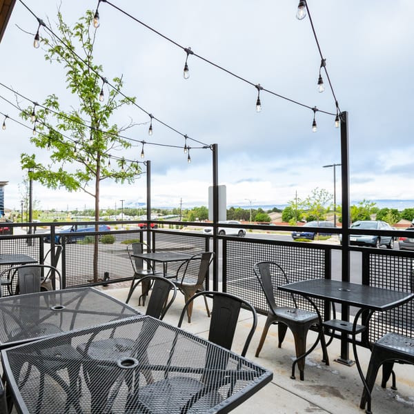 Outdoor patio of Skirted Heifer with metal tables, chairs, string lights, and a view of the street.