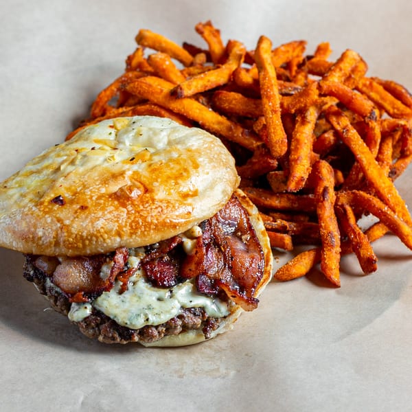 A Skirted Heifer burger with bacon and melted cheese, served with a side of sweet potato fries.