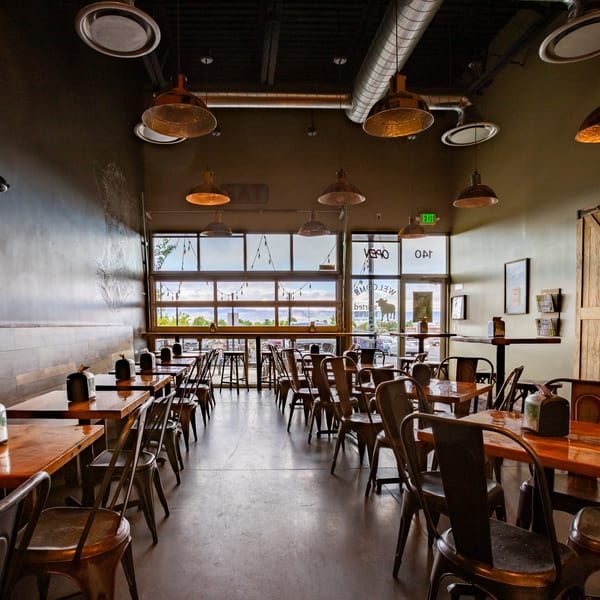 Interior of Skirted Heifer restaurant with empty tables, chairs, and large windows overlooking mountains.