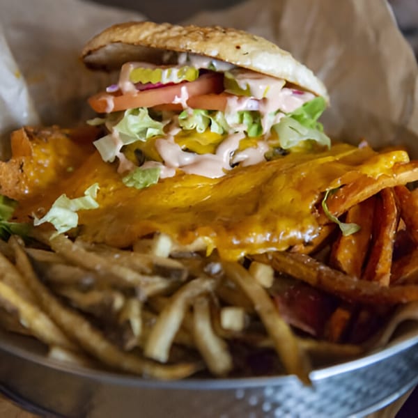 A Skirted Heifer burger with melted cheese, lettuce, tomato, pickles, and sauce, served with fries.