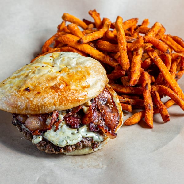 A Skirted Heifer burger with bacon and melted cheese, served with a side of sweet potato fries.
