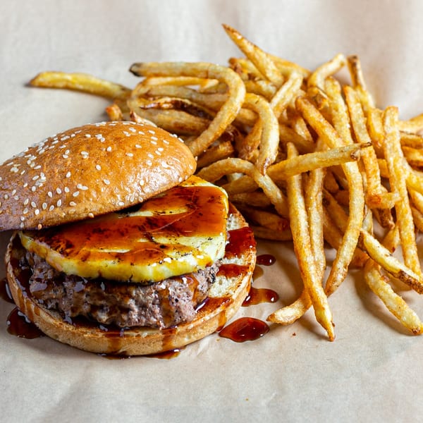 A Skirted Heifer burger with grilled pineapple and sauce, served with a side of crispy fries.