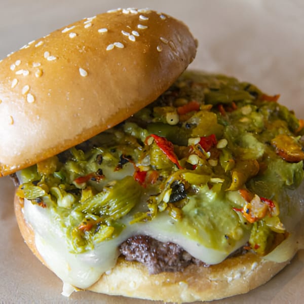 A Skirted Heifer burger with melted cheese and green chili relish on a sesame seed bun.