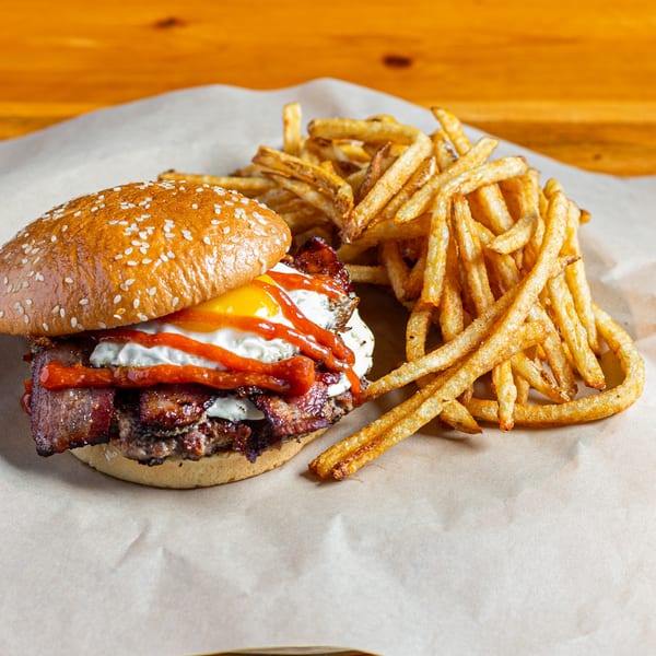 A Skirted Heifer burger with bacon, egg, and sauce, served with a side of fries.