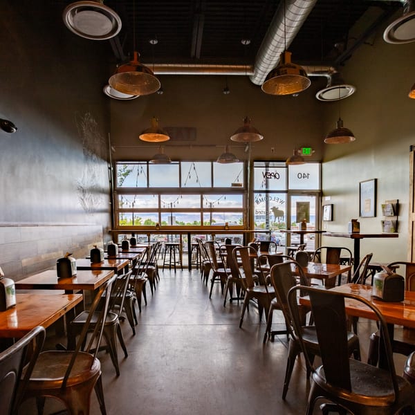 Interior of Skirted Heifer restaurant with empty tables, chairs, and large windows overlooking mountains.