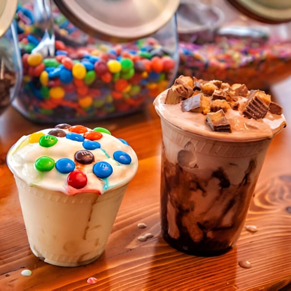 Two milkshakes, one with M&M's and one with Reese's, on a wooden table.