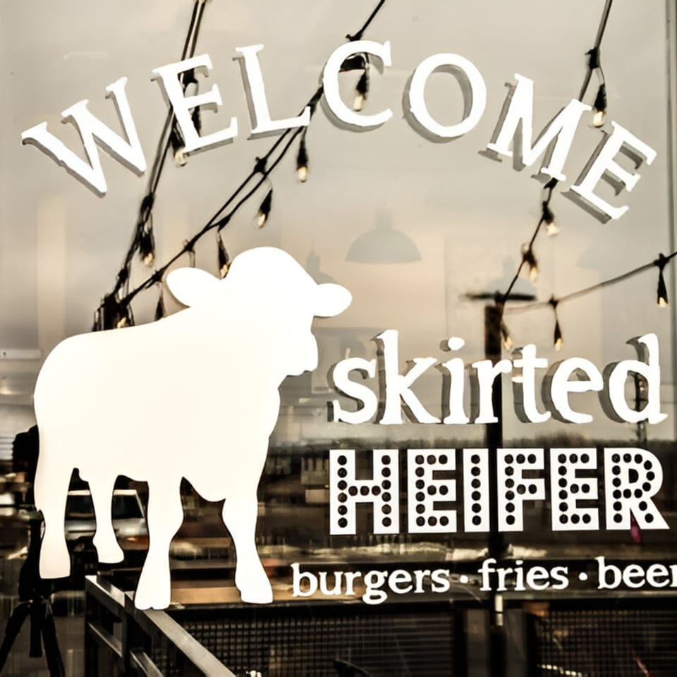 The Skirted Heifer restaurant window with "WELCOME" and a cow silhouette, advertising "burgers fries beer".