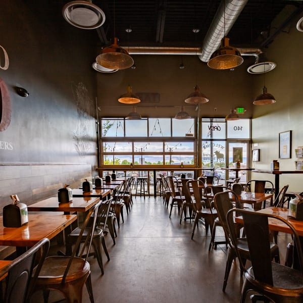 Interior of Skirted Heifer restaurant with empty tables, chairs, and large windows overlooking a landscape.