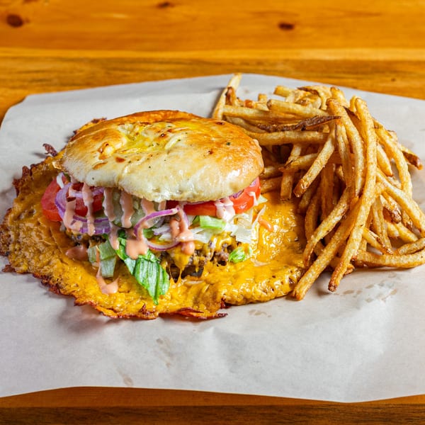 A Skirted Heifer burger with a cheese skirt, lettuce, tomato, onion, and sauce, with fries.
