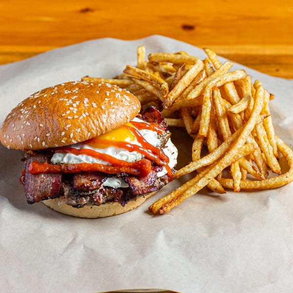 A Skirted Heifer burger with bacon, fried egg, and ketchup, served with a side of fries.