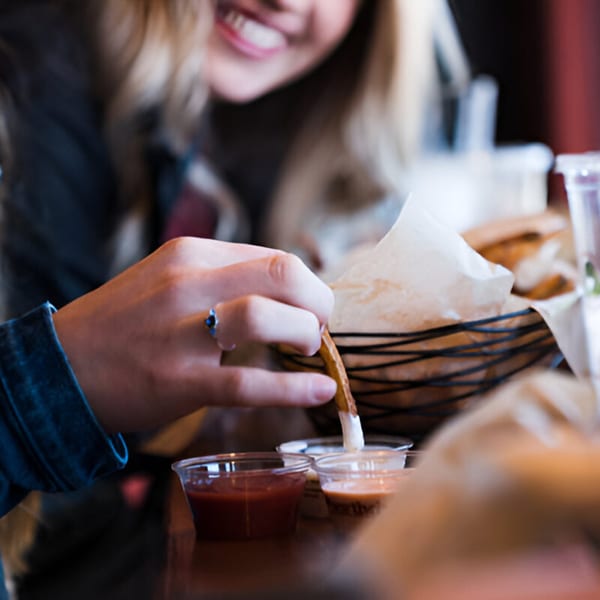 A person dips a Skirted Heifer french fry into a small cup of dipping sauce.