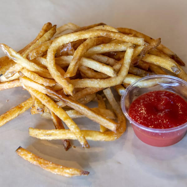 A pile of golden-brown Skirted Heifer fries with a side of ketchup in a plastic cup.